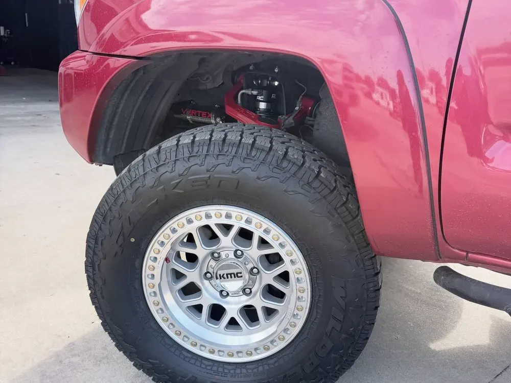 Close-up of a silver KMC wheel and all-terrain tire under a lifted red Tacoma