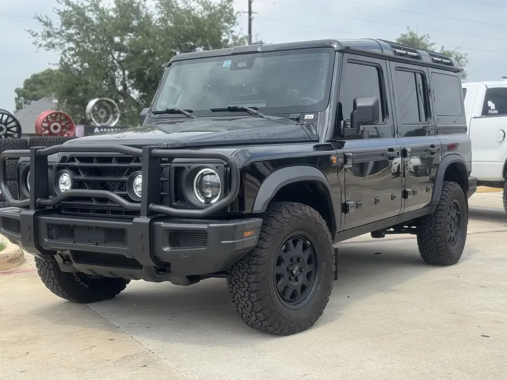 Black boxy 4x4 SUV with a grille guard on black off-road wheels and all-terrain tires