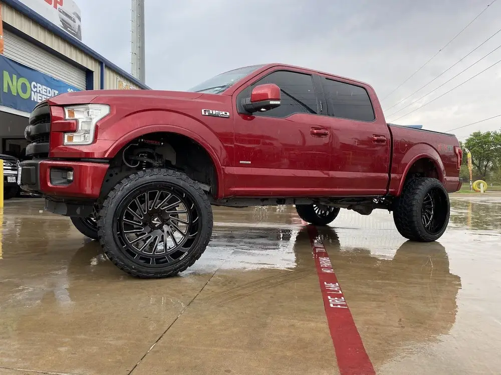 Lifted red Ford F-150 on large black custom wheels and off-road tires