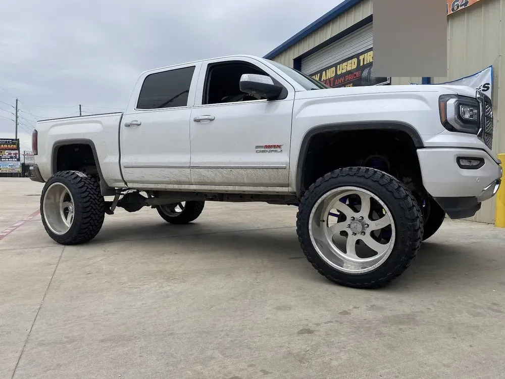 Lifted white GMC Sierra Denali on brushed aftermarket wheels and mud-terrain tires