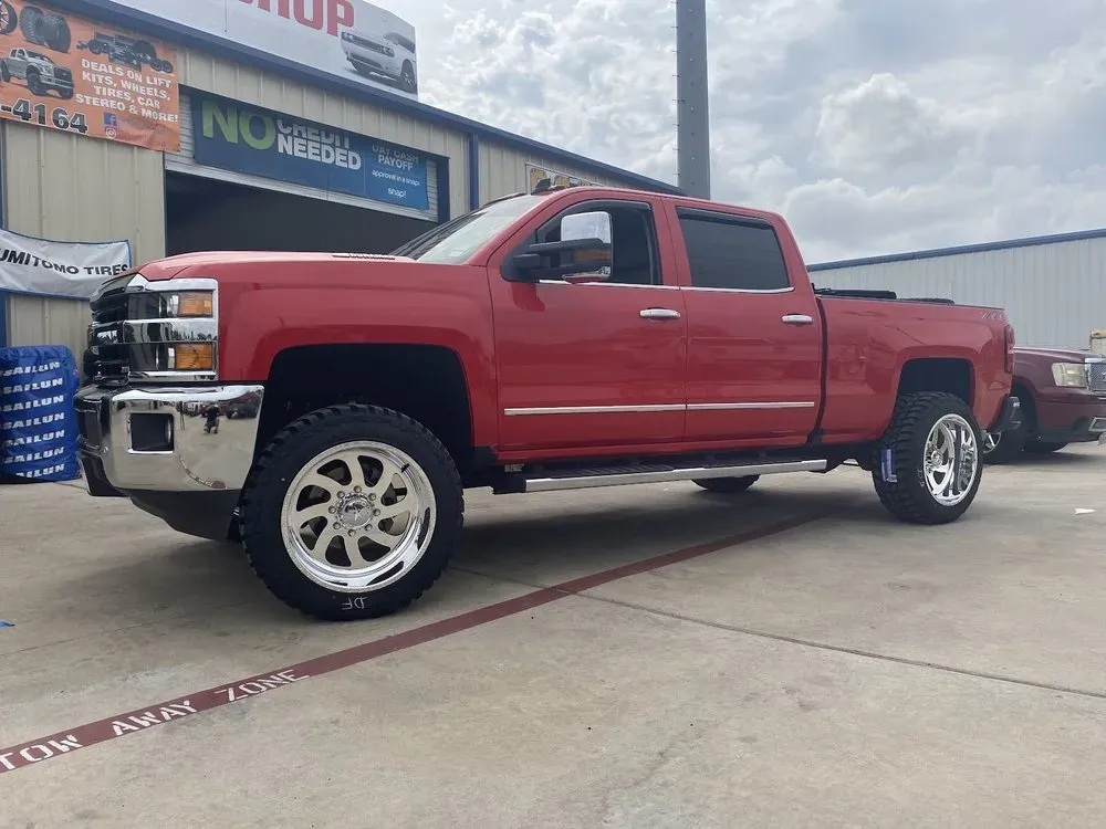 Leveled red Chevrolet Silverado HD on polished custom wheels outside the tire shop