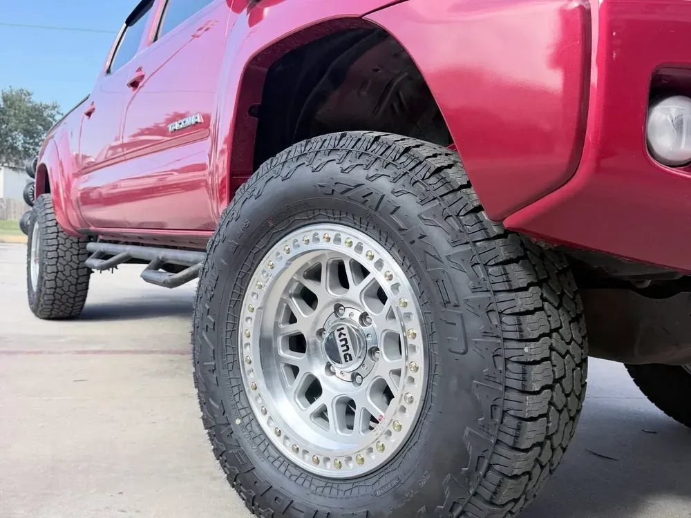 Red Toyota Tacoma on silver beadlock-style KMC wheels and all-terrain tires
