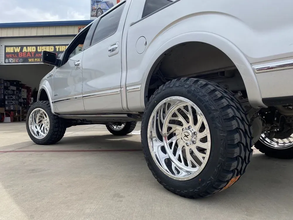 Close view of a lifted silver Ford F-150 on polished custom wheels and mud tires